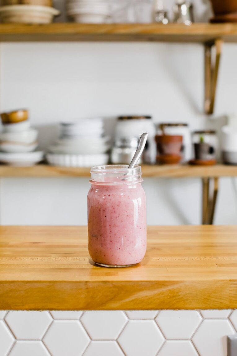 Strawberry and peach smoothie in a mason jar on a kitchen countertop.