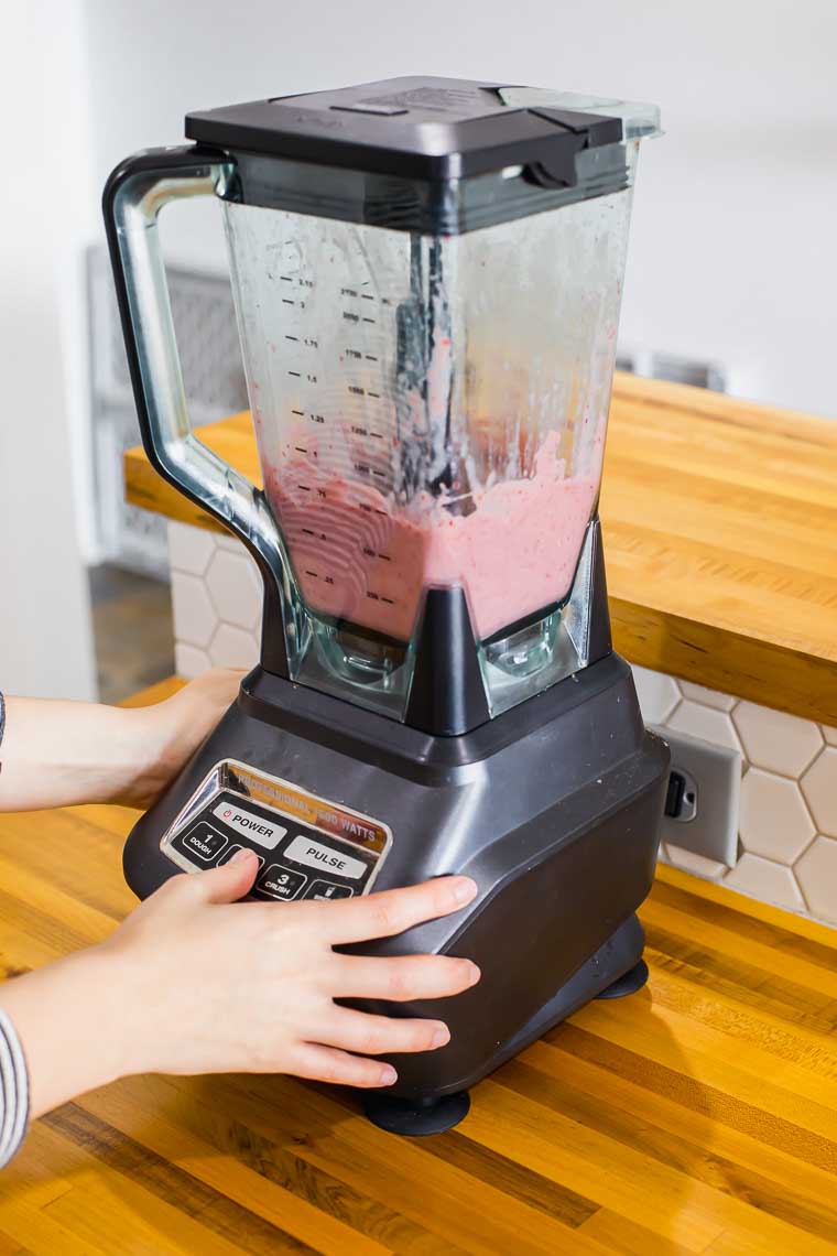 Woman's hands blending a strawberry smoothie.