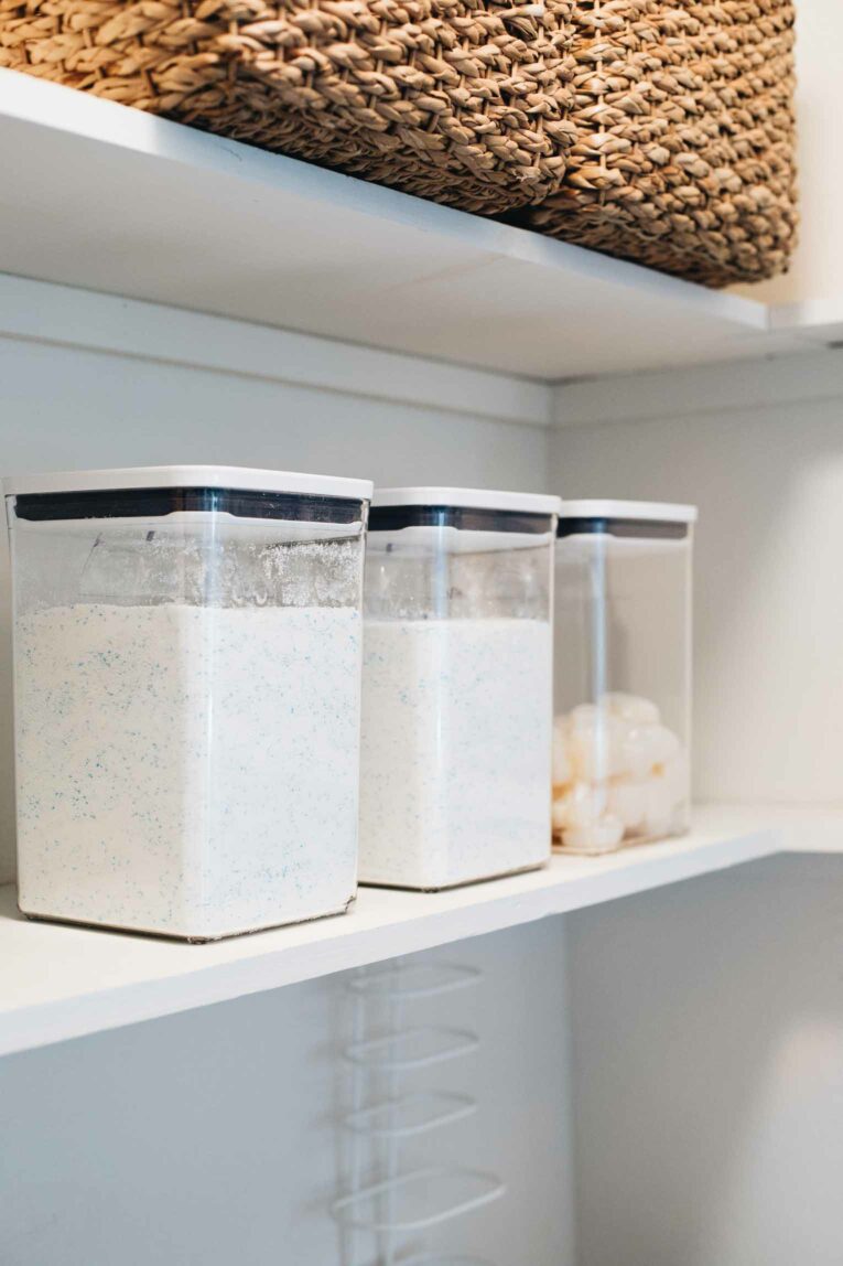 Side shot of 3 clear OXO POP containers with dry detergent on a white shelf.