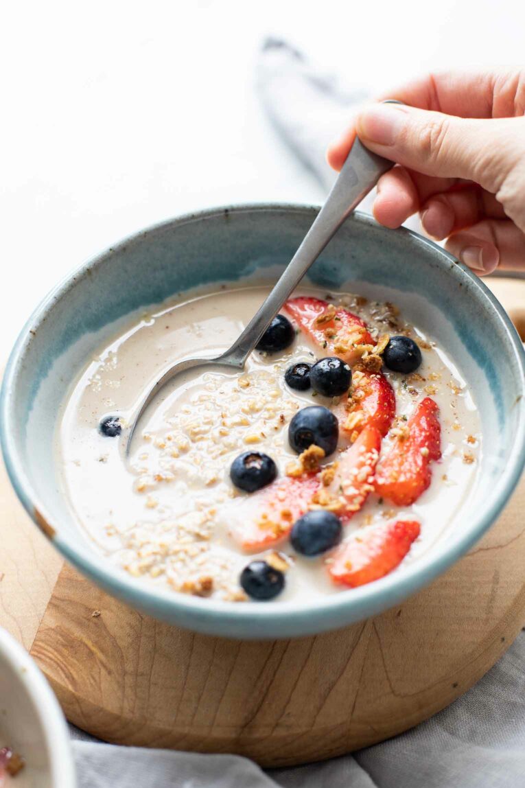 Angled shot of steel cut oats with berries, milk, a spoon, and a hand scooping it out.
