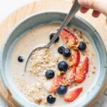 Top shot of overnight steel cut oats in a blue bowl topped with berries, milk, and a spoon.