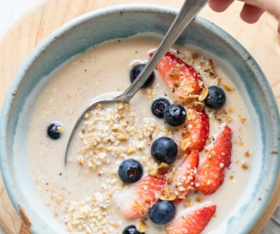 Top shot of overnight steel cut oats in a blue bowl topped with berries, milk, and a spoon.