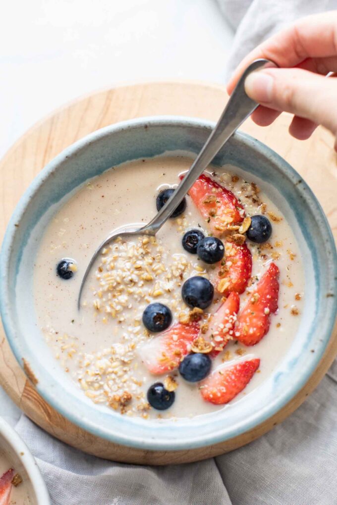 Top shot of overnight steel cut oats in a blue bowl topped with berries, milk, and a spoon.