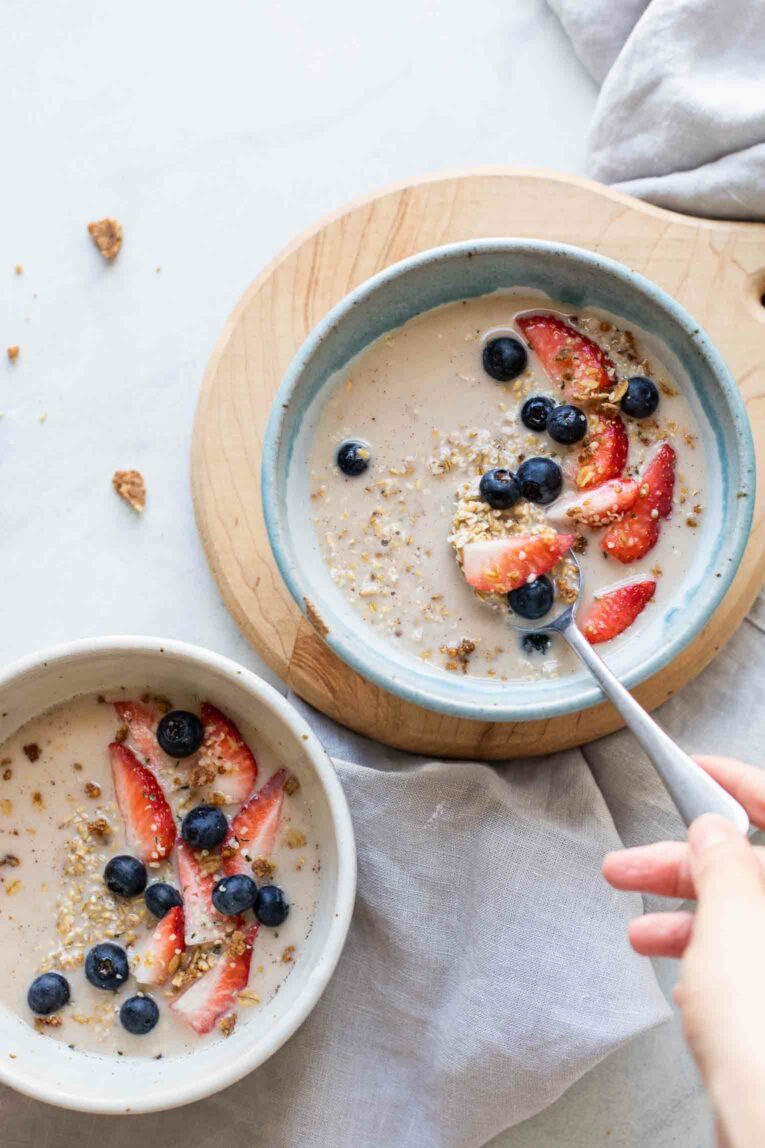 Two bowls of overnight steel cut oats with berries and a hand with a spoon.