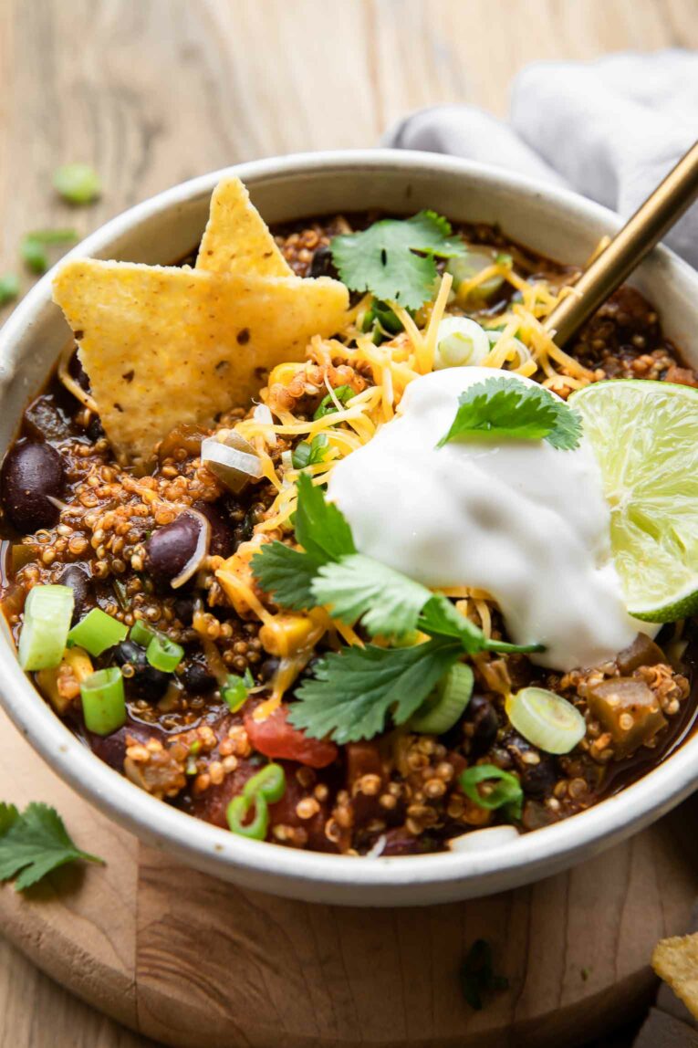 Angled shot of quinoa chili in a white bowl with sour cream and tortilla chips.