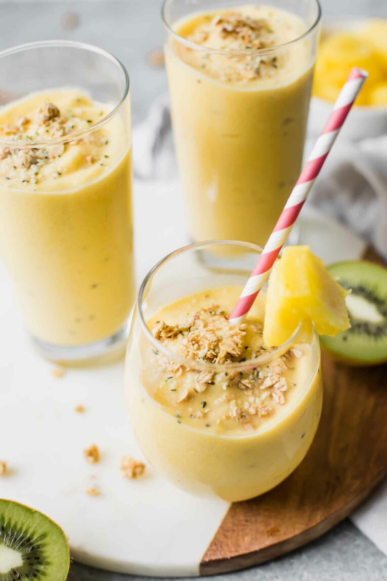 Angled shot of smoothies with pineapple, coconut, and mango on a marble cutting board.