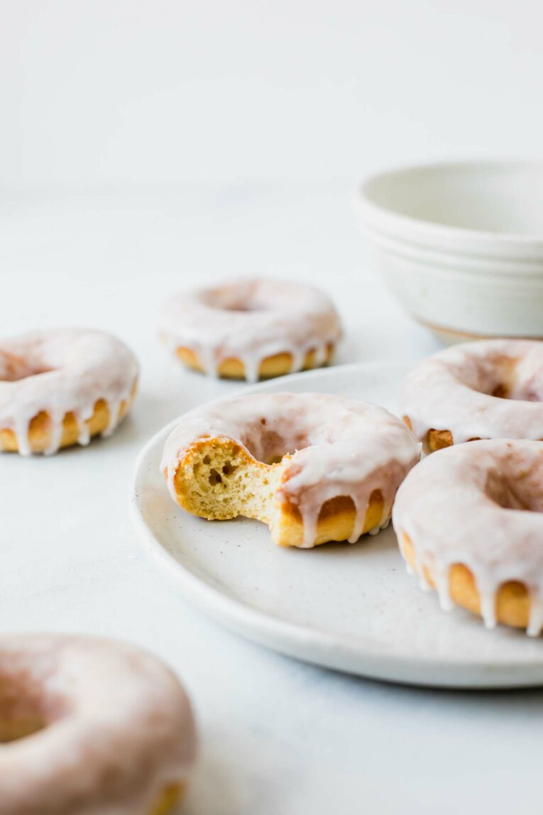 Glazed doughnuts on a white plate with a bite taken out.