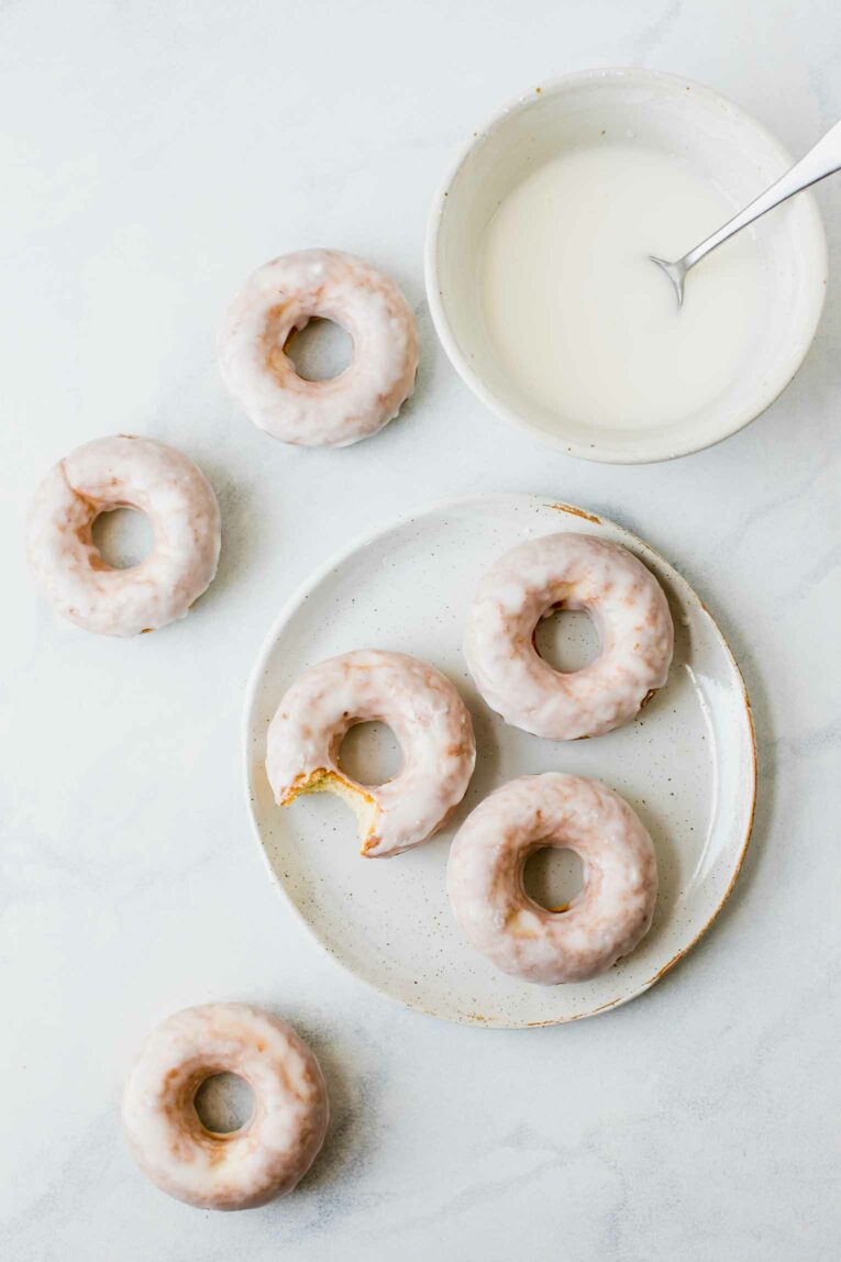Top shot of glazed doughnuts on a plate with a bowl of icing.