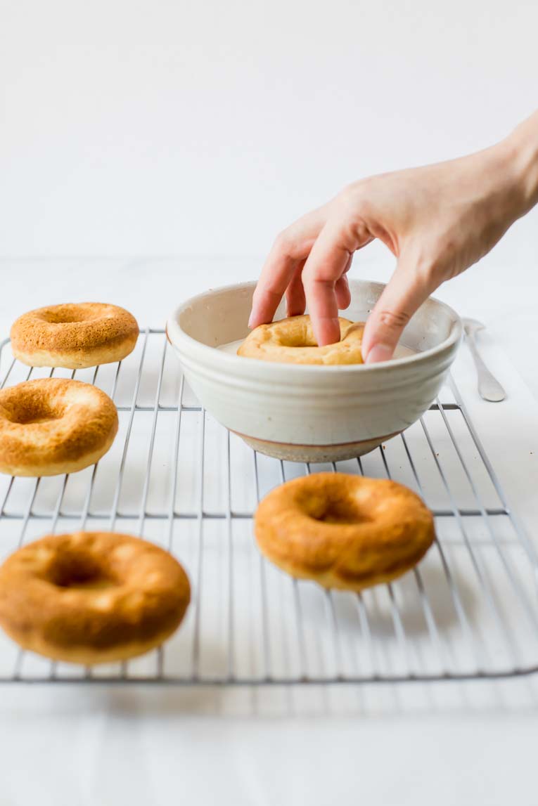 Baked doughnut being dipped in glaze.