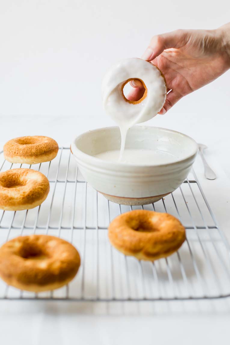 Doughnut freshly dipped in a white bowl of glaze.