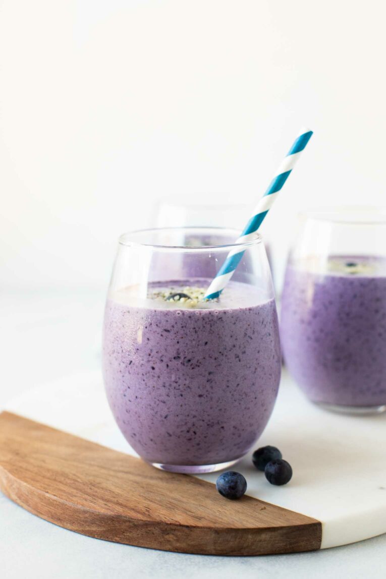 Blueberry Keto Smoothie in a glass cup with a blue striped straw.
