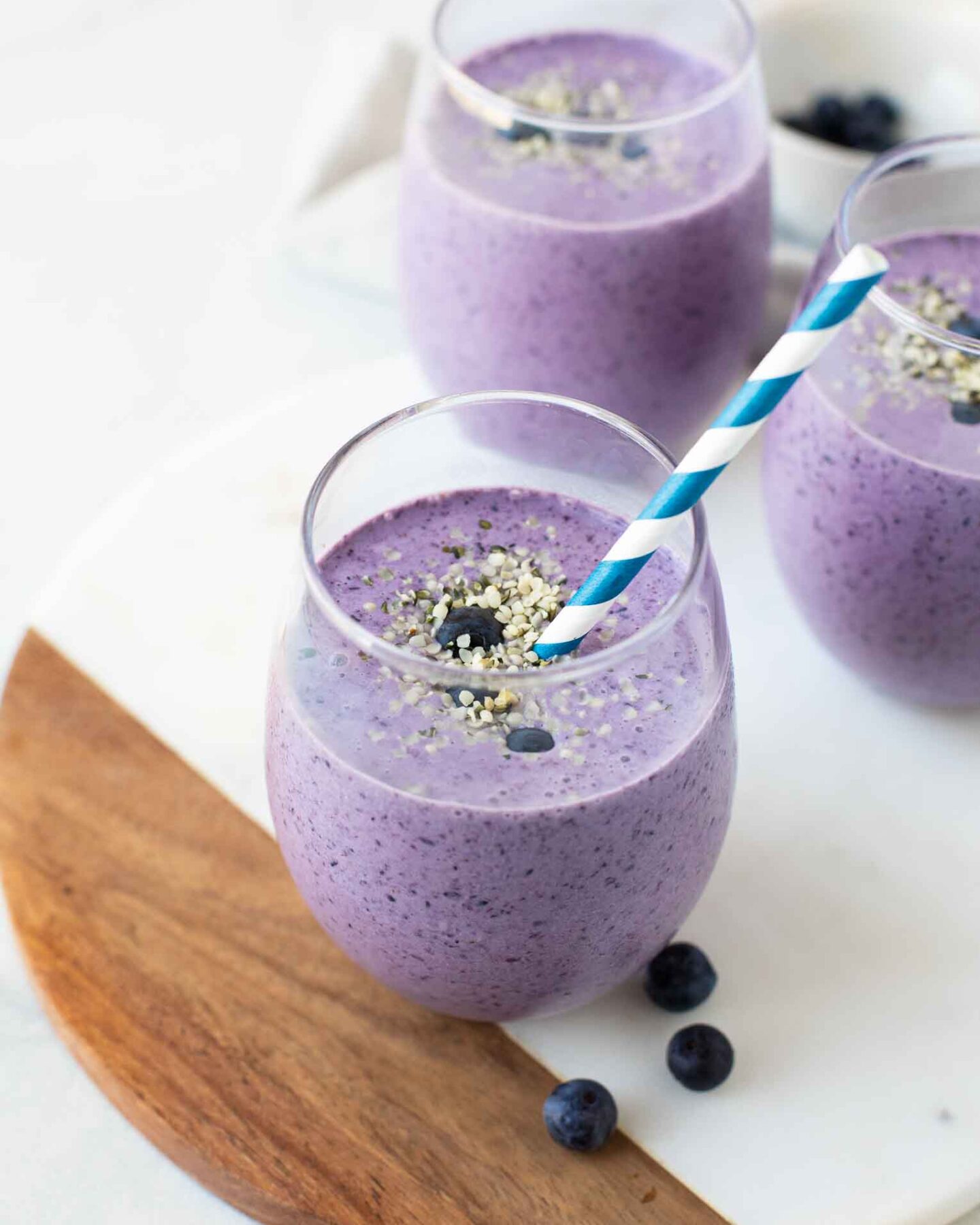 Angled shot of a blueberry keto smoothie in a glass cup with a straw.