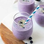Angled shot of a blueberry keto smoothie in a glass cup with a straw.