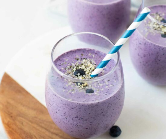 Angled shot of a blueberry keto smoothie in a glass cup with a straw.