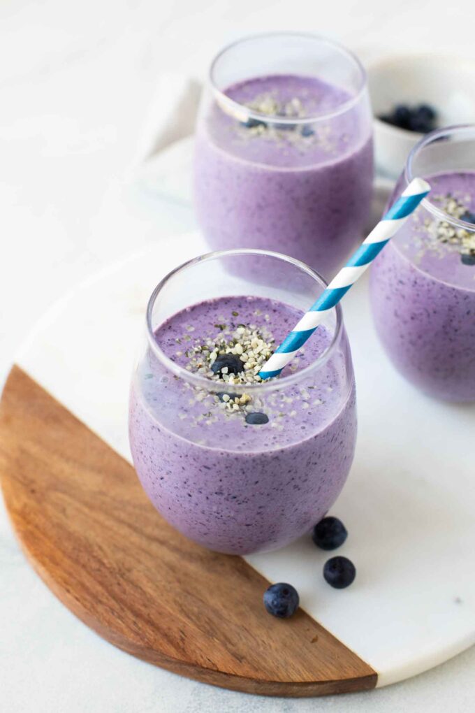 Angled shot of a blueberry keto smoothie in a glass cup with a straw.
