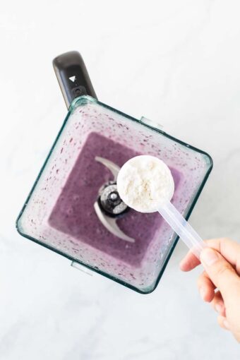 Blueberry smoothie in a blender with a scoop of Keto supplement.