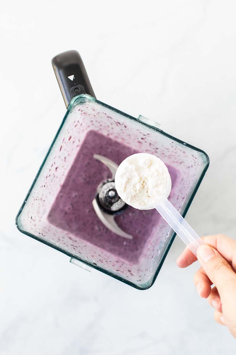 Blueberry smoothie in a blender with a scoop of Keto supplement.