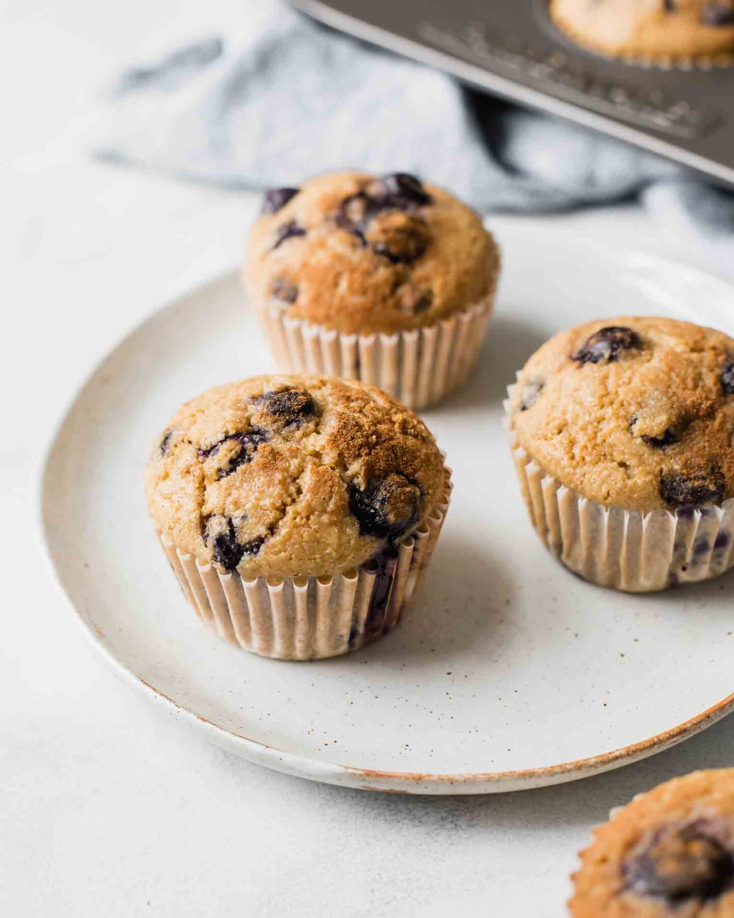Angled shot of Blueberry Quinoa Muffins on a white plate with a napkin in the background.