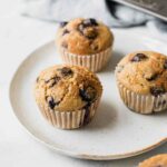 Angled shot of Blueberry Quinoa Muffins on a white plate with a napkin in the background.