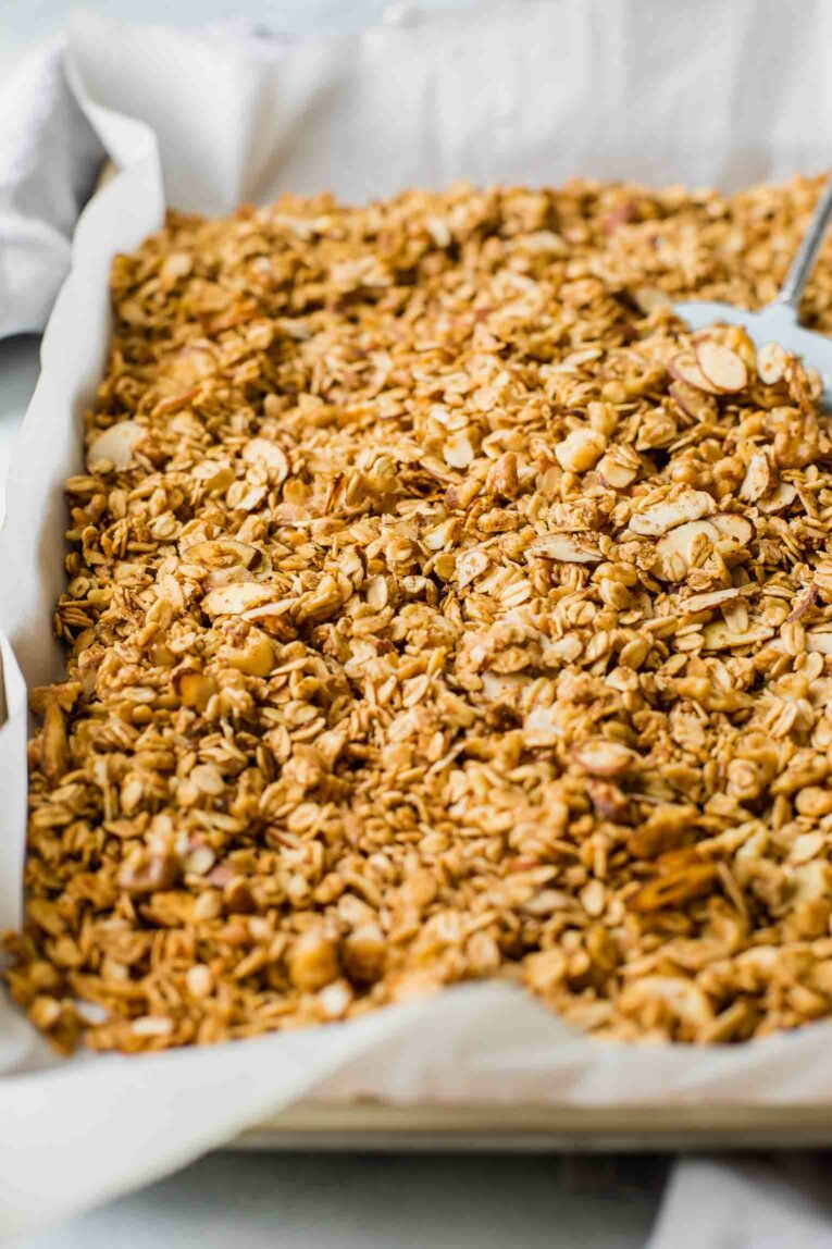 Baked granola in a baking sheet lined with parchment paper.