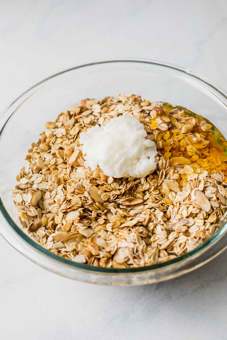 Liquid ingredients over dry ingredients for granola in a glass mixing bowl.
