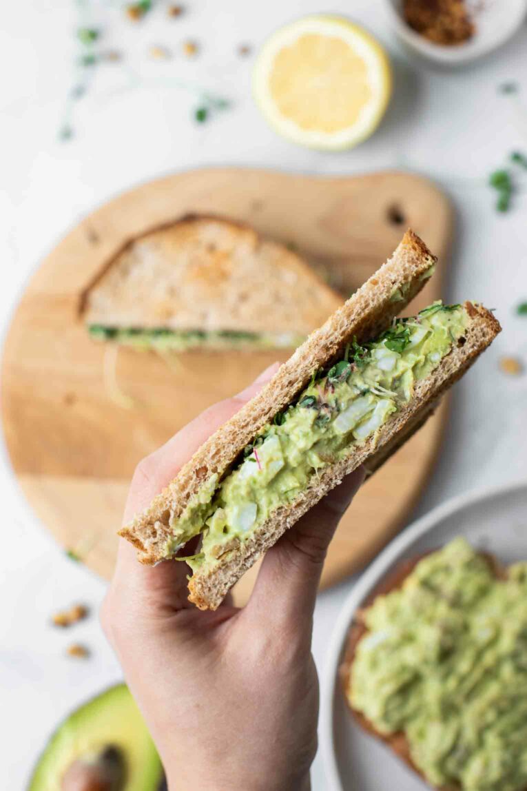 Close up of hand holding Avocado Egg Salad sandwich.