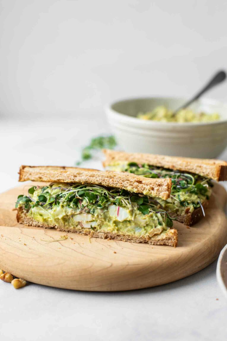 Across shot of an avocado egg salad sandwich on a cutting board.