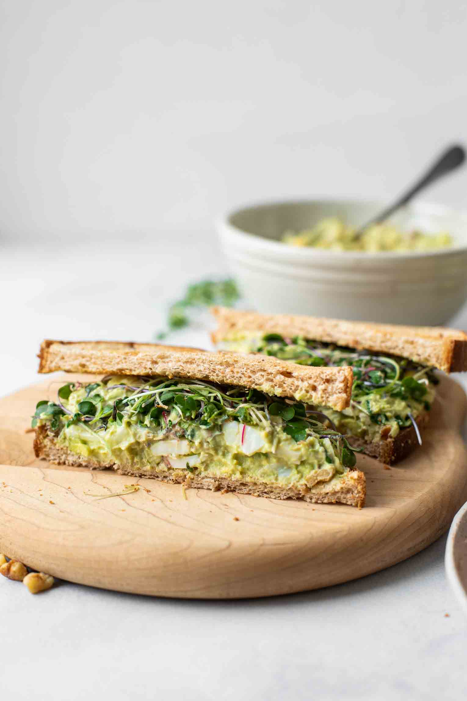 Across shot of an avocado egg salad sandwich on a cutting board.