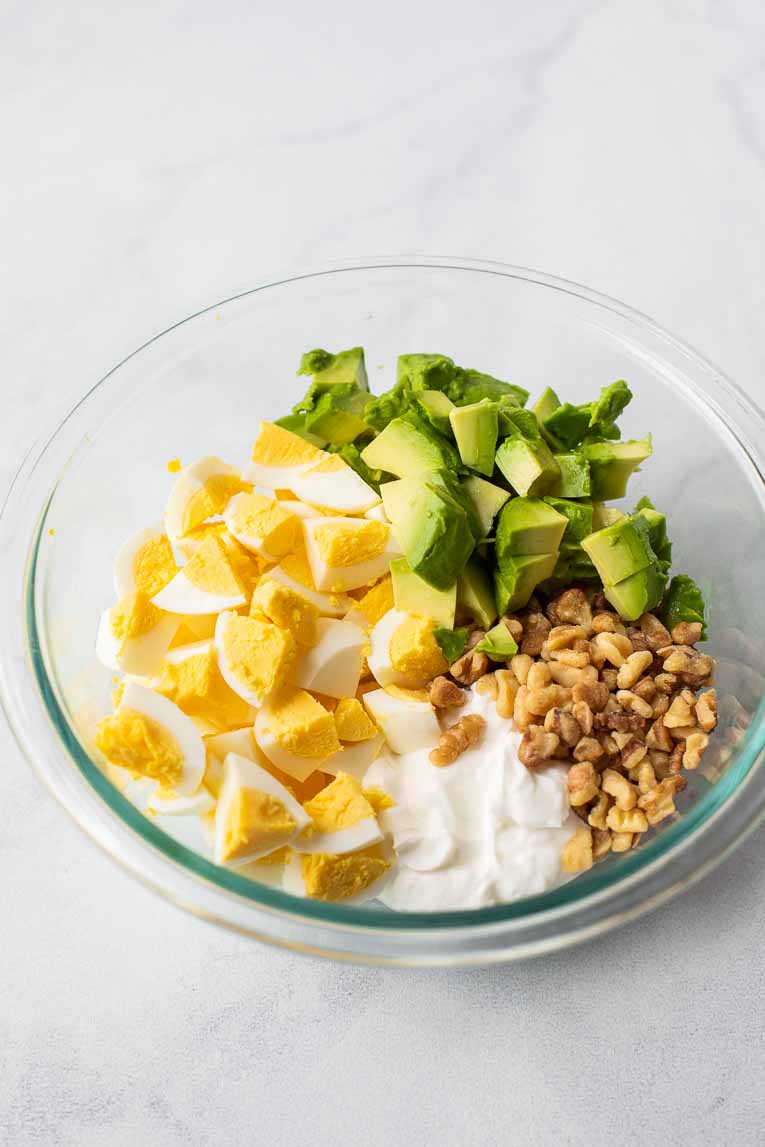 Glass bowl with eggs, avocado, yogurt, and walnuts.
