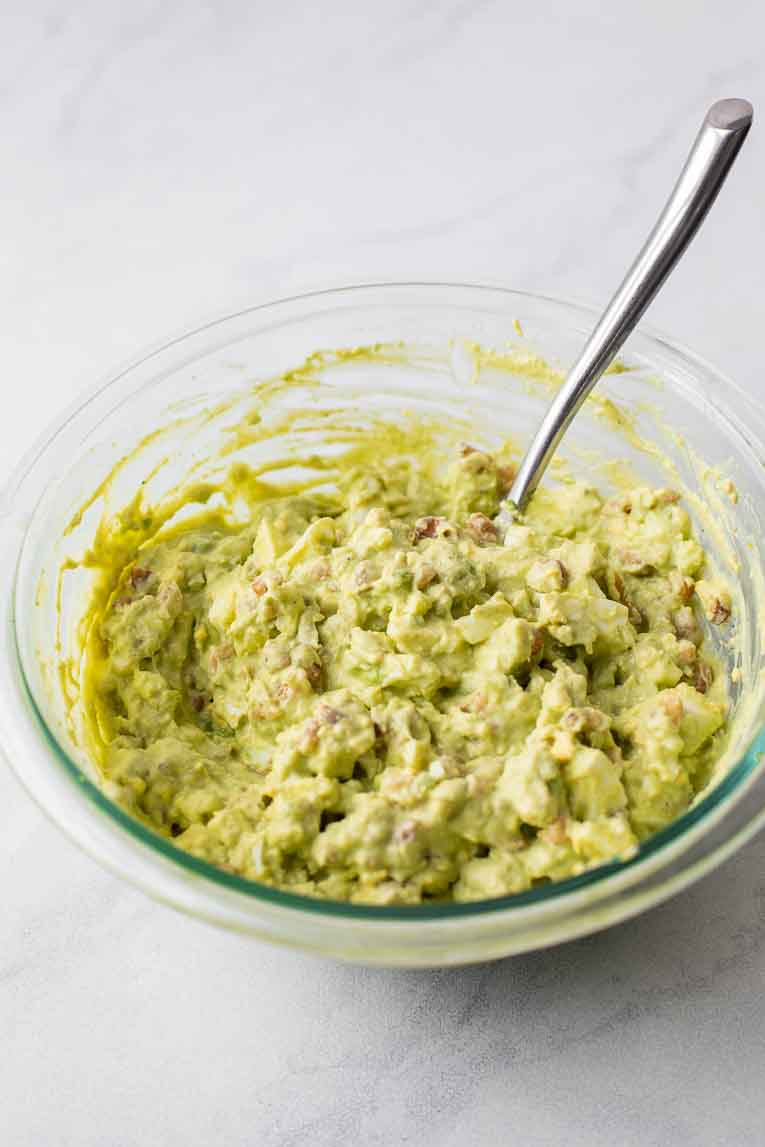 Mashed avocado egg salad in a glass bowl.