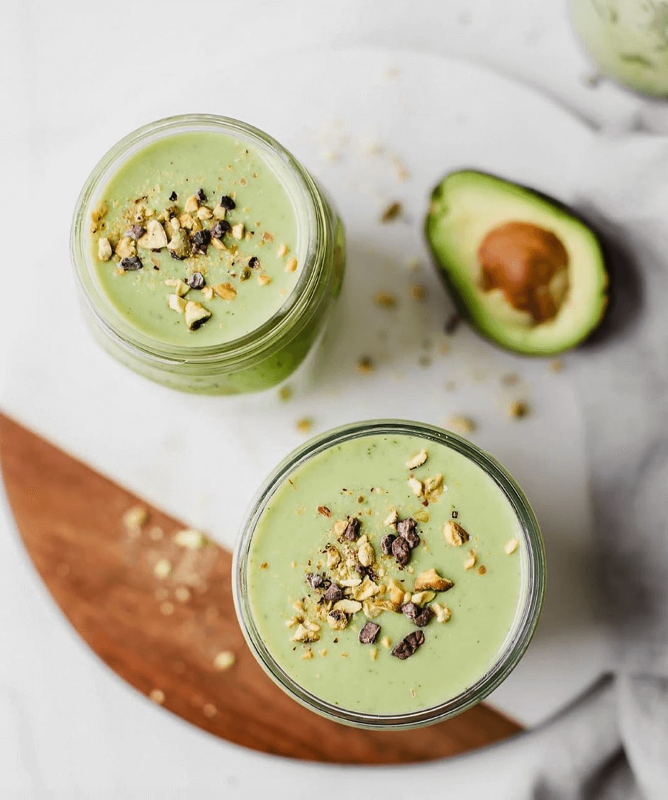 2 green smoothies on a cutting board next to half an avocado