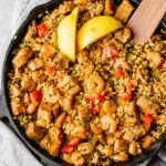 Chicken, shrimp, rice, and tomatoes with lemon slices in a skillet.