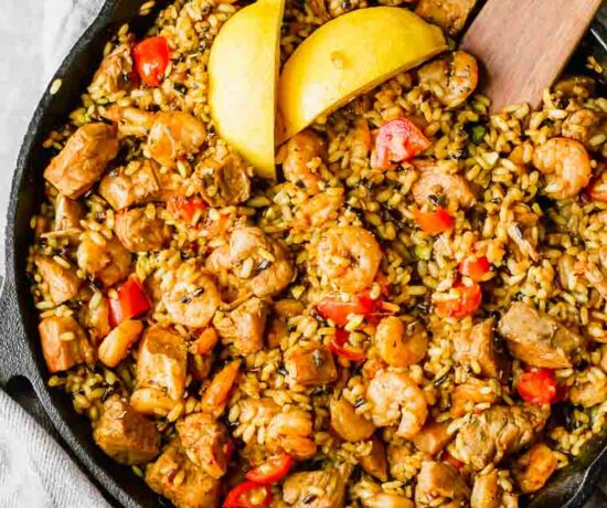 Chicken, shrimp, rice, and tomatoes with lemon slices in a skillet.