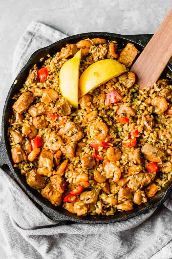 Chicken, shrimp, rice, and tomatoes with lemon slices in a skillet.