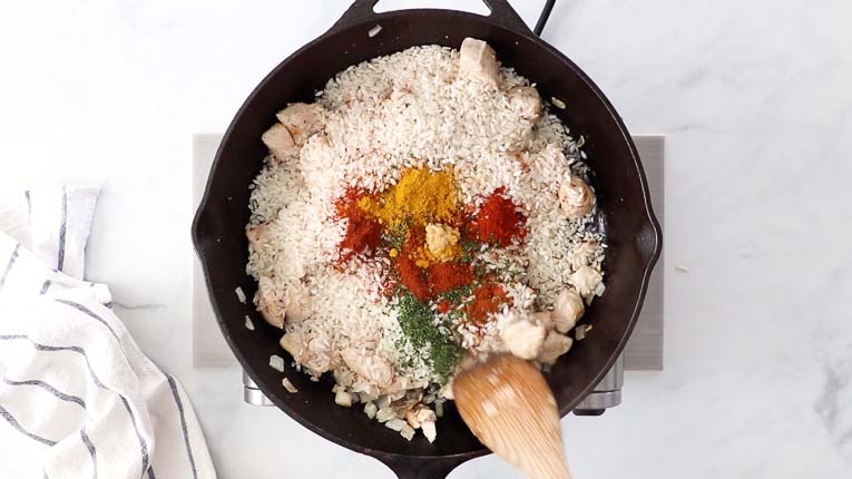 Chicken, rice, and spices cooking in a cast iron skillet.