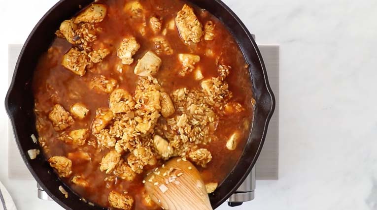 Chicken with broth, rice, and spices cooking in a skillet.