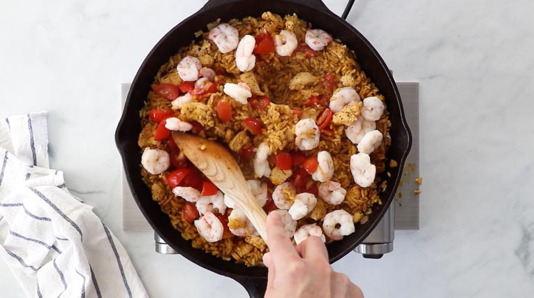 Shrimp and tomatoes added to chicken and rice in a skillet.