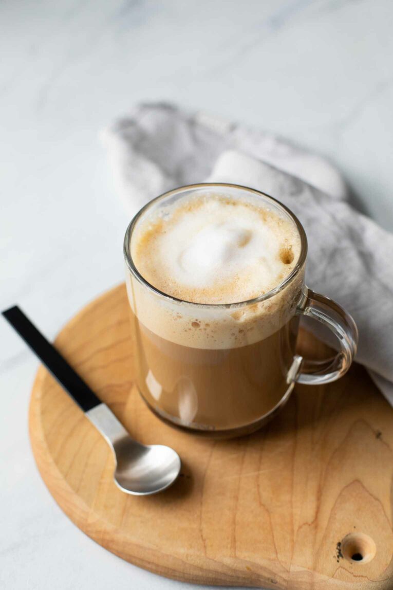 Vanilla latte recipe in a glass mug over a wooden cutting board.