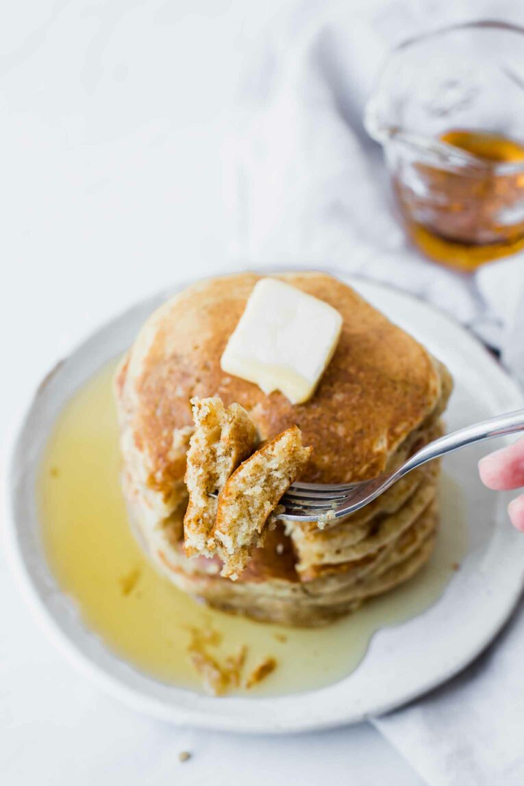 Fork cutting into a stack of pancakes with butter and syrup.
