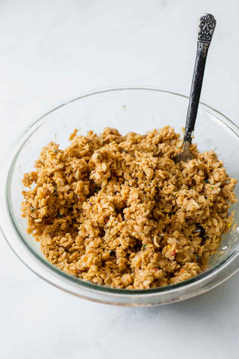 Glass mixing bowl with rice cereal, honey, cashew butter, and sprinkles.