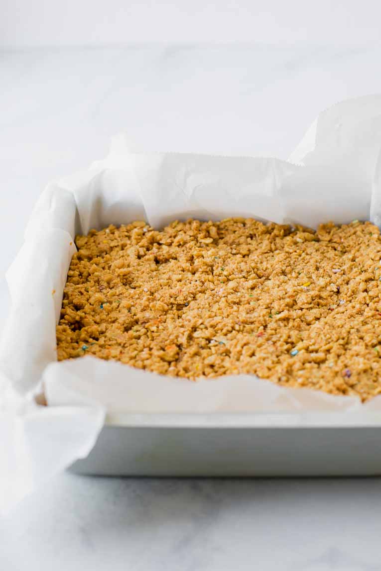 Rice krispies in a cake pan lined with parchment paper.