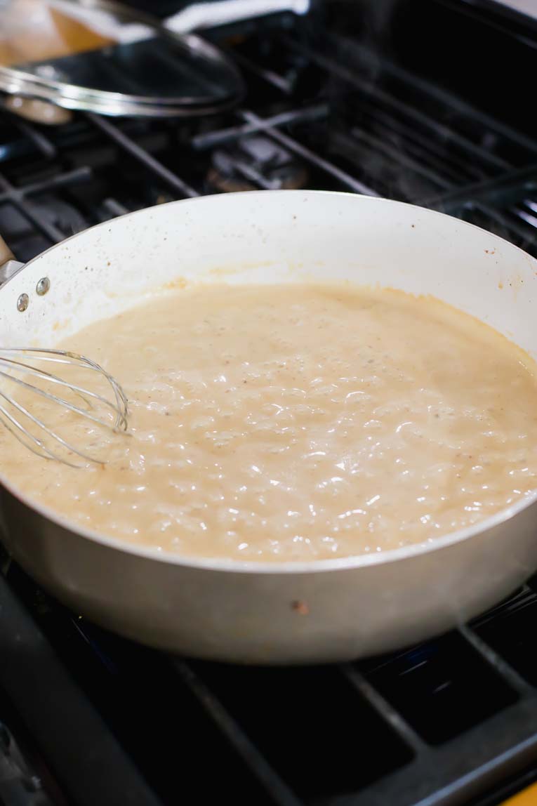 Swedish meatball sauce being simmered and whisked in a saucepan.