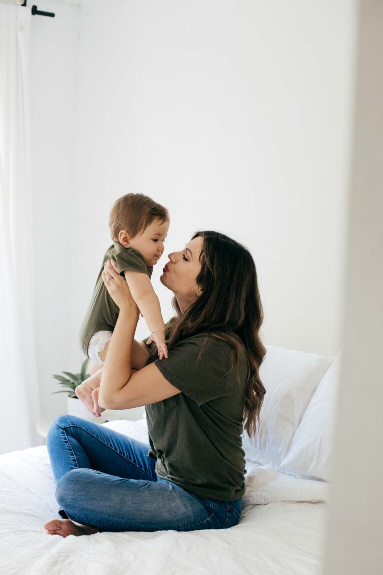 Mother holding baby up and kissing him.