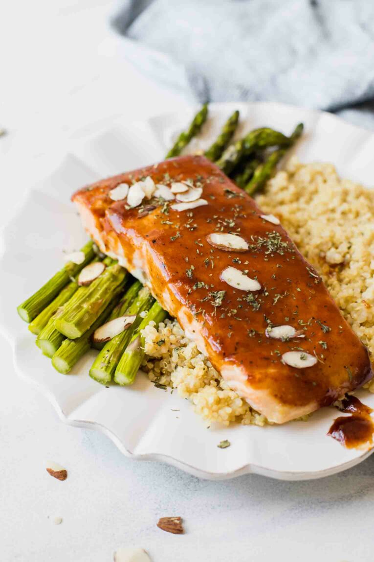 Angle shot of baked barbecue salmon on a white plate with quinoa and asparagus.