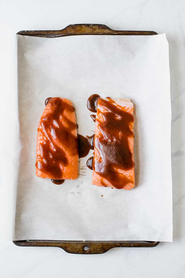 Two salmon filets covered in barbecue sauce on a baking sheet.