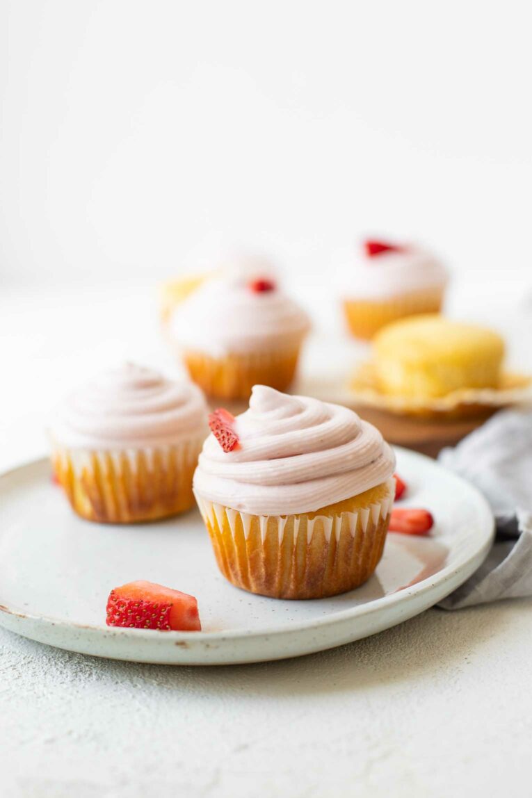 Across shot of Strawberry Lemonade Cupcakes on a white plate with strawberries.