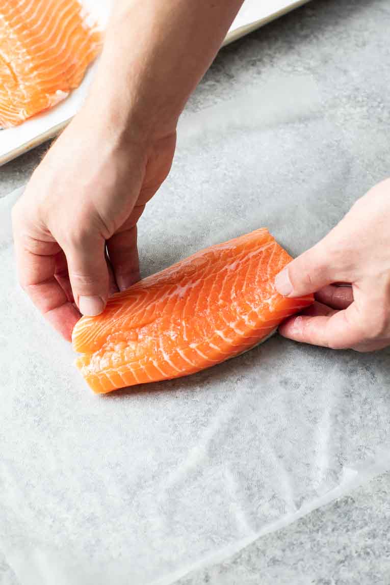 Hands putting salmon filet on plastic wrap.
