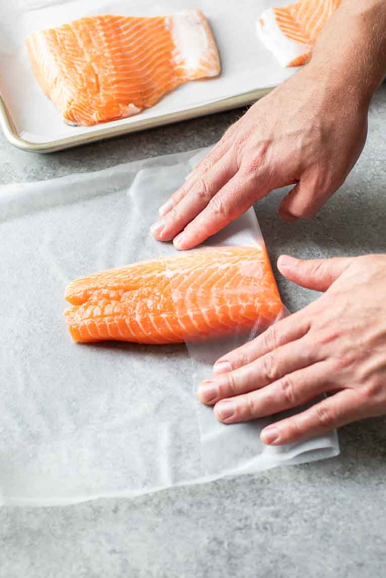 Folding plastic wrap over salmon filet.