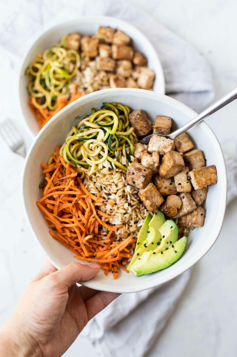 Hand holding Asian Tofu Rice Bowl with fork.