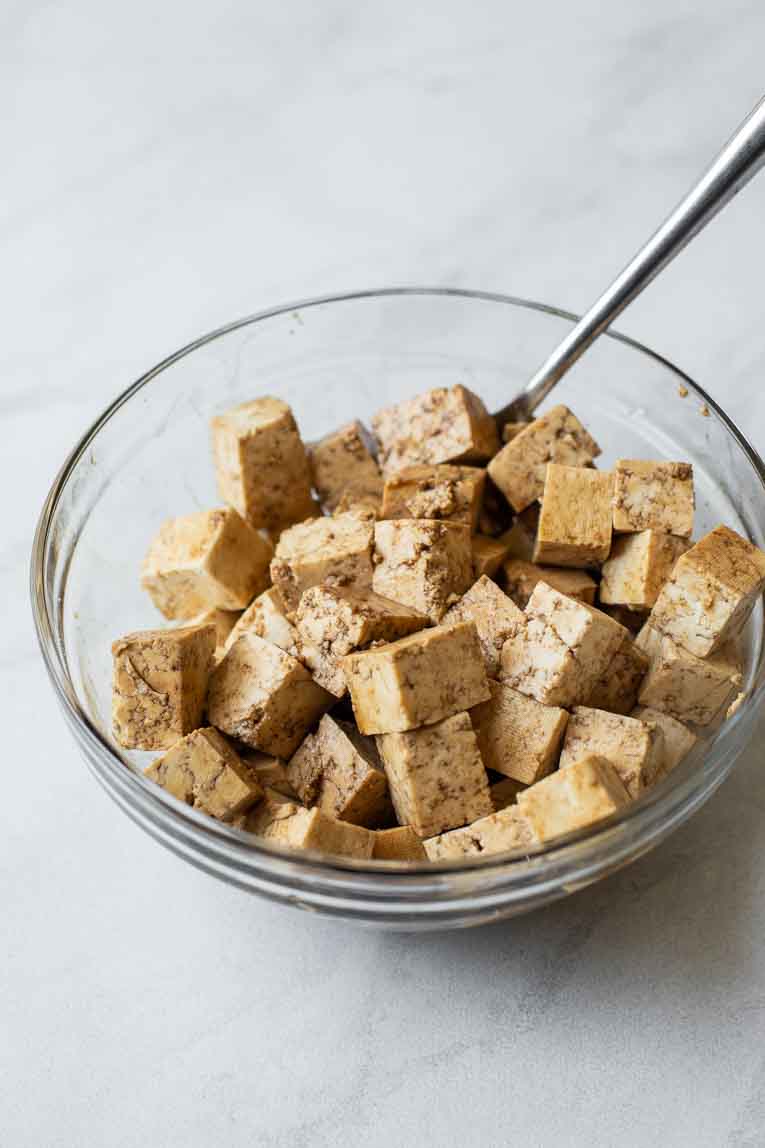 Tofu soaked in an Asian sauce in a glass bowl.